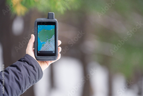 Tourist navigator in a shockproof rubberized case in a man's hand on a blurry background of a winter forest. On the screen is a map of the area and waypoints.