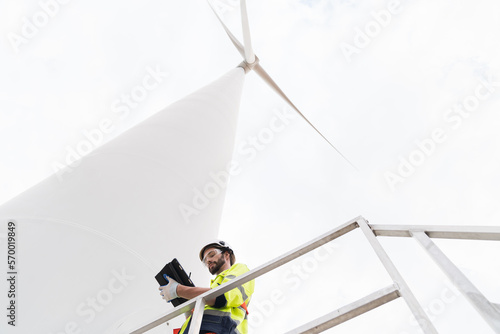 Male engineer working with plan inspecting or maintenance of wind turbines at windmill field farm. Male engineer using computer tablet control or monitoring wind turbine system at wind turbines farm