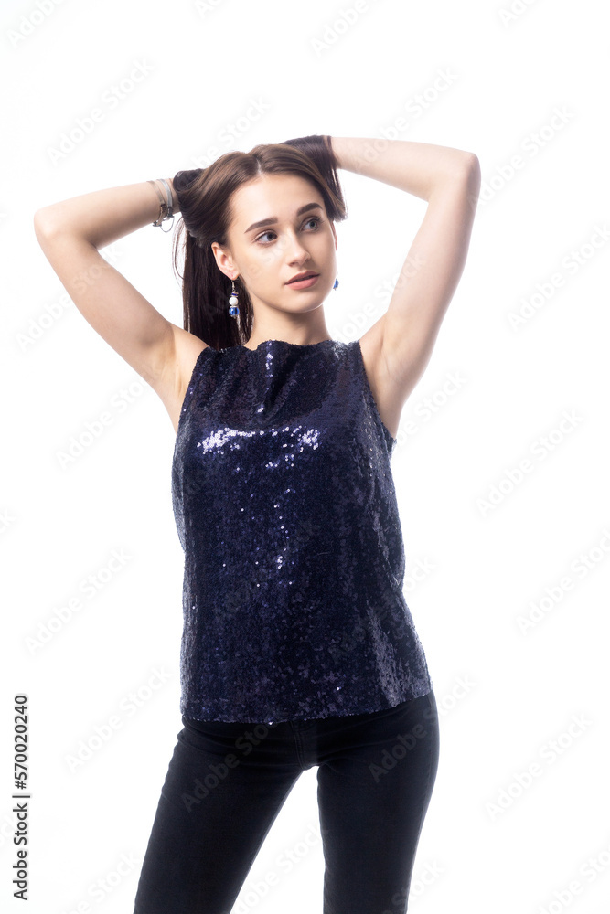 A young woman with dark hair in a dark blue sequined top holds her hair with her hands on a white background A young woman with dark hair in a dark blue sequined top holds her hair with her hands on a white background