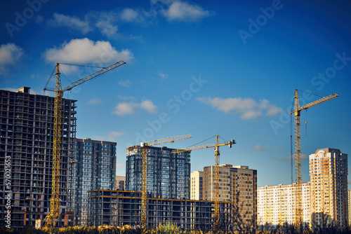 Group of tower cranes on the construction site against blue sky. Cranes for construction of high-rise buildings. Real estate construction. Concept of urban development and architecture.