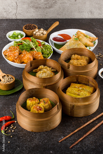 Assorted asian food set. fried dim sum, fried spring rolls, fried indian samosa and fried tofu with salt and pepper on dark rustic background.