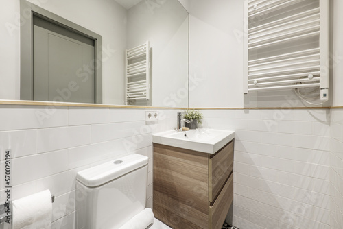 Newly renovated bathroom white porcelain sink on wooden cabinet with drawers  heated towel rail  integrated wall mirror with wooden border and decorative plant