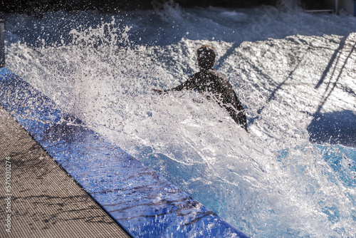 A surfer in the water giving it a go in a wave pool with big splashes in the turns and sunlit drops everywhere
