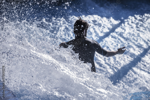 A surfer giving it a go in a wave pool with big splashes in the turns and sunlit drops everywhere
