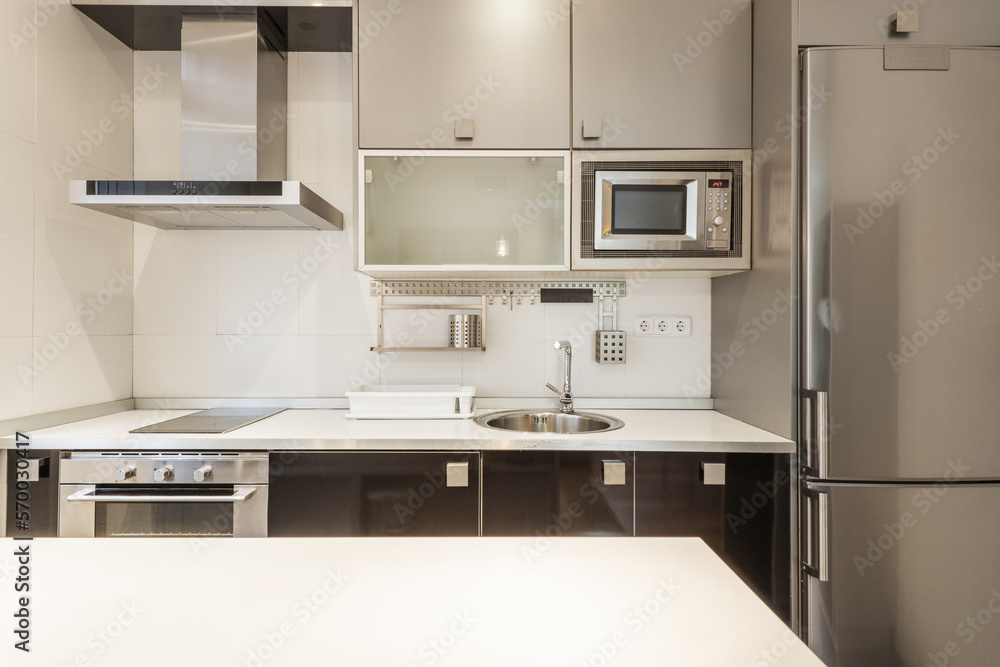 Open kitchen furnished with base units in gloss black, white countertop with aluminum edge and wall units in gray with integrated appliances in a study Open kitchen furnished with base units in gloss black, white countertop with aluminum edge and wall units in gray with integrated appliances in a study