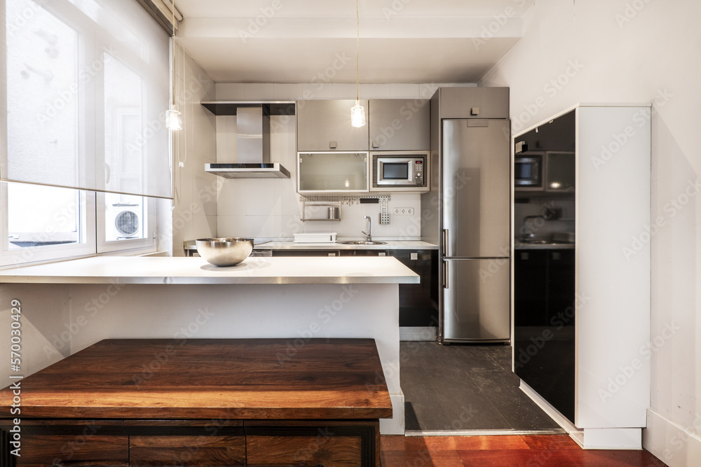 Open kitchen furnished with base units in gloss black, white countertop with aluminum edge and wall units in gray with integrated appliances in a studio apartment Open kitchen furnished with base units in gloss black, white countertop with aluminum edge and wall units in gray with integrated appliances in a studio apartment