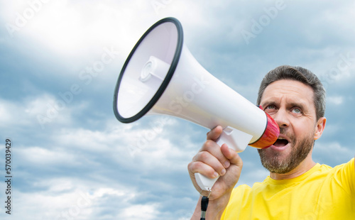 man in yellow shirt shout in loudspeaker on sky background. copy space © be free