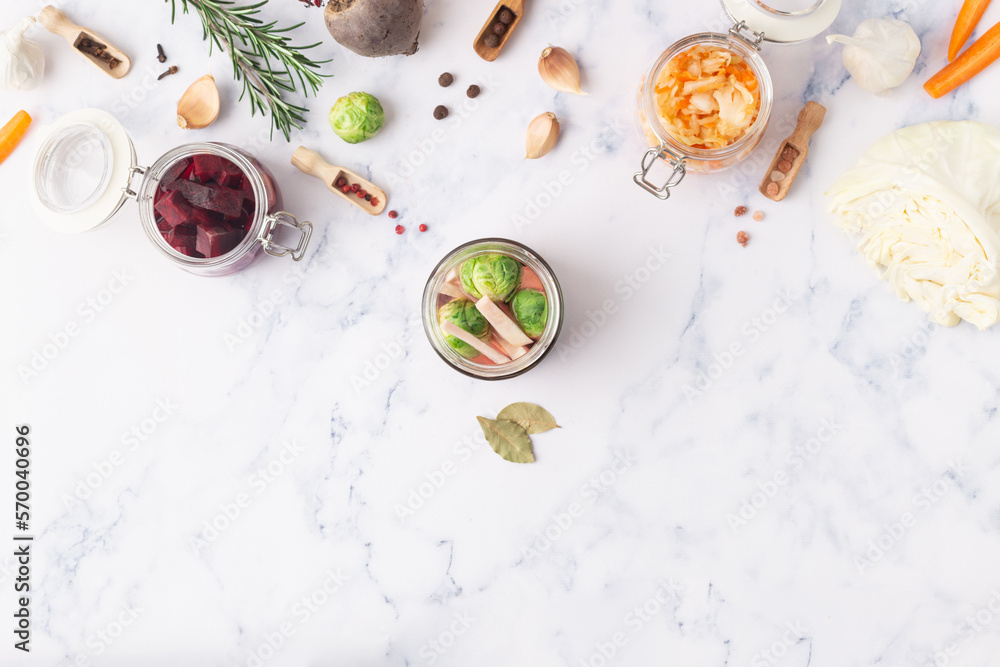 Glass jars with various pickled vegetables and ingredients on a marble background Glass jars with various pickled vegetables and ingredients on a marble background