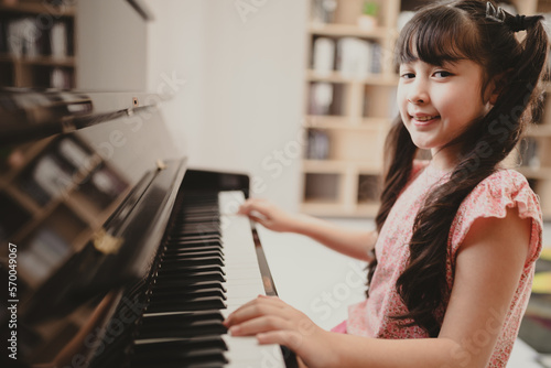 Cute and focused young little Asian girl practicing songs and melody while pressing white and black key and creating new music on piano as hobby and dedication at home