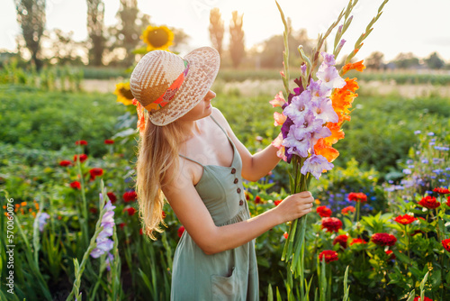 Portrait of young woman gardener enjoying bunch of fresh gladiolus in summer garden. Farmer picked bouquet of flowers