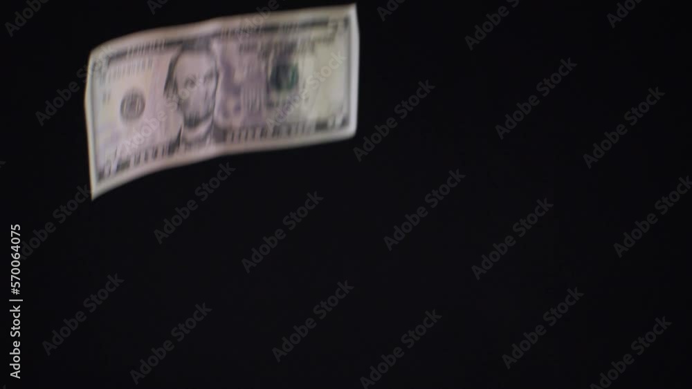 Dollars of different values fall in front of the camera lens in slow motion on a black isolated background. Different dollar bills fall down in the rain. The concept of money falling from the sky. Dollars of different values fall in front of the camera lens in slow motion on a black isolated background. Different dollar bills fall down in the rain. The concept of money falling from the sky.