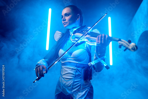 Beautiful violinist girl playing violin on stage with neon light and smoke