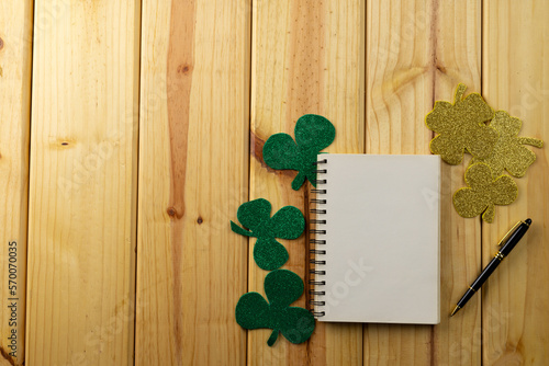 Image of green clover and white notebook with copy space on wooden background