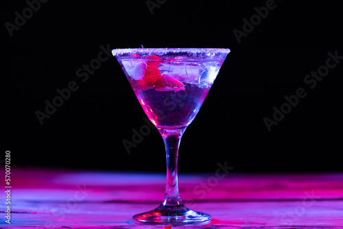 Glass with water and diverse fruits in neon light with copy space over black background