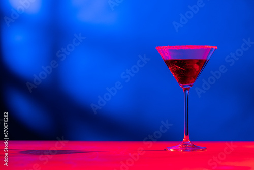 Glass with cocktail and diverse fruits in neon light with copy space over blue background