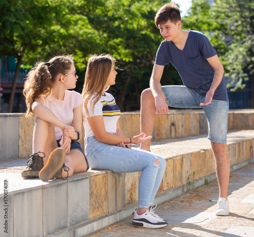 Teenagers have fun talking on the street, discussing photos on the smartphone screen