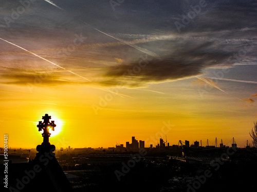 Silhouette of stone crucifix on top of church with Manchester City centre in background 