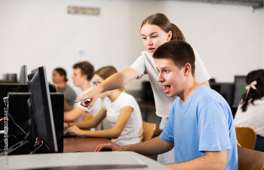 Positive young boy and girl using personal computer together, enjoying computer game.