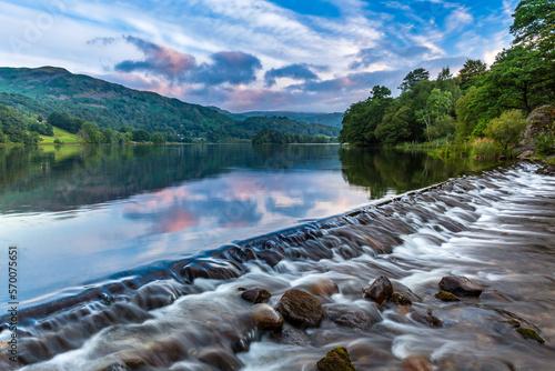 The River Rothay flowing over the weir at Grasmere Lake towards Rydal and on to Windermere in the Lake District National Park. A lovely morning sky over the Barrowdale fells in the distance. photo