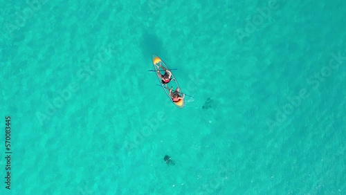 Drop down aerial drone shoto of a clear see through kayak with two people floating along the carribean sea in clear blue water. photo