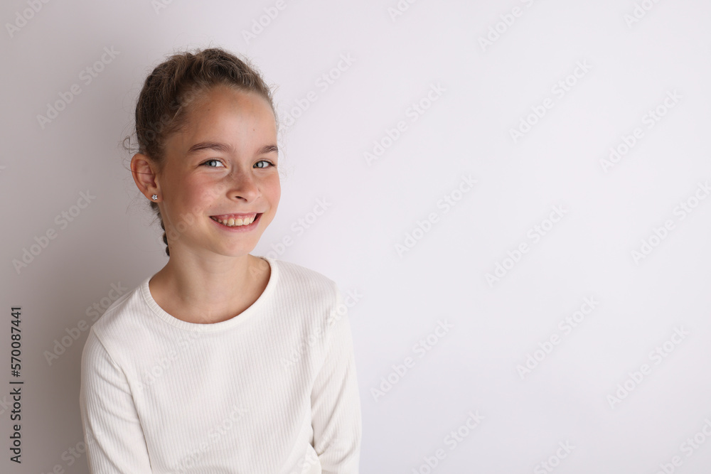 Little emotional teen girl in white shirt 11, 12 years old on an isolated white background. Children's studio portrait. Place text, to copy space for inscription, advertising children's goods.