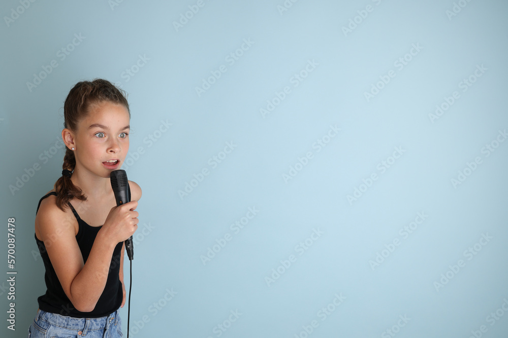 Portrait of a cute teenage girl singing, using microphone. Teenage girl in black t-shirt on an isolated blue background. Karaoke for kids, home entertainment for kids. Singer singing with microphone. Portrait of a cute teenage girl singing, using microphone. Teenage girl in black t-shirt on an isolated blue background. Karaoke for kids, home entertainment for kids. Singer singing with microphone.