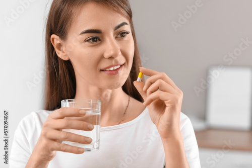 Beautiful woman with vitamin supplement and glass of water in kitchen, closeup