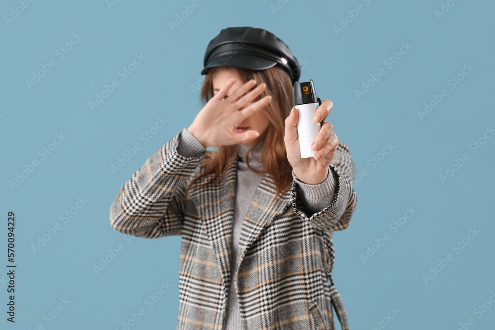 Scared young woman with pepper spray for self-defence on blue background Scared young woman with pepper spray for self-defence on blue background
