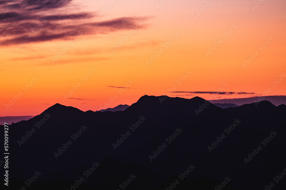 horizontal photo of silhouettes of mountains below the sun in the golden hour 