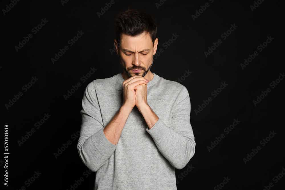Man with clasped hands praying on black background Man with clasped hands praying on black background