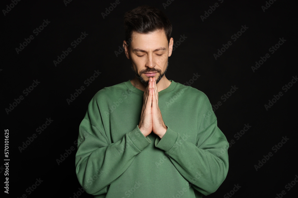 Man with clasped hands praying on black background Man with clasped hands praying on black background