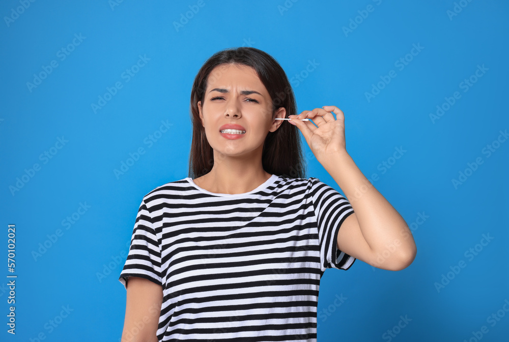 Young woman cleaning ear with cotton swab on light blue background Young woman cleaning ear with cotton swab on light blue background
