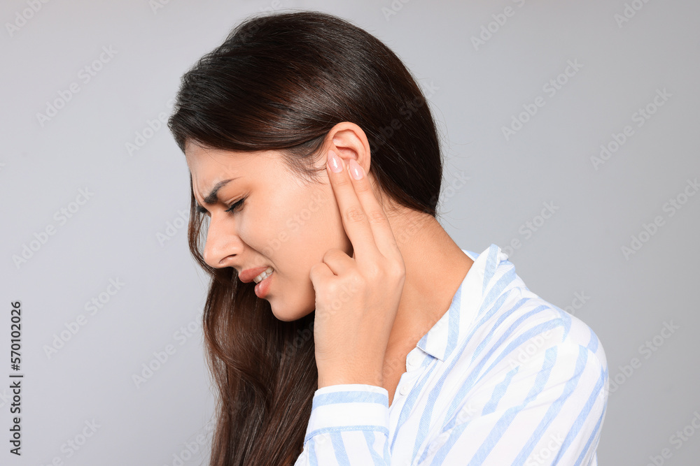 Young woman suffering from ear pain on light grey background Young woman suffering from ear pain on light grey background