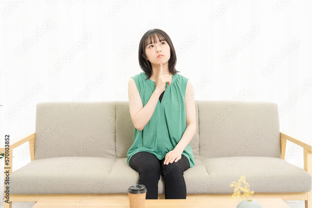 ソファに座って考え事をしている若い女性 ソファに座って考え事をしている若い女性