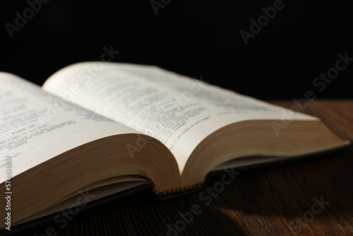 Open Bible on wooden table against black background, closeup