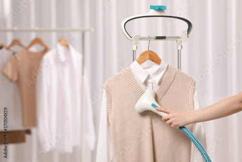 Woman steaming clothes on hanger at home, closeup. Space for text