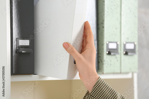 Woman taking folder with documents from shelf, closeup
