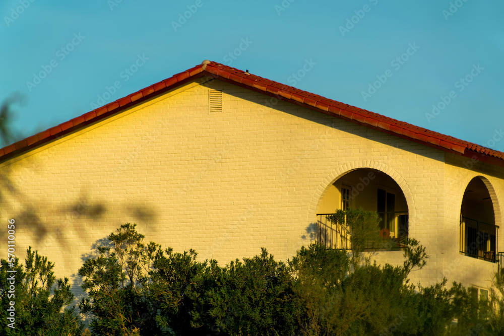 Desert building with dark blue sky with front or back yard trees on gable style brick roof with red tiles and balconies Desert building with dark blue sky with front or back yard trees on gable style brick roof with red tiles and balconies