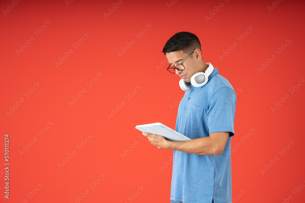 Young man wearing glasses, reading on a digital tablet and wearing headphones on his neck Young man wearing glasses, reading on a digital tablet and wearing headphones on his neck