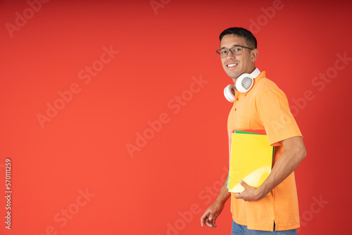 Young male student with glasses, posing in profile looking at the camera carrying his notebooks and headphones © Guillermo Spelucin