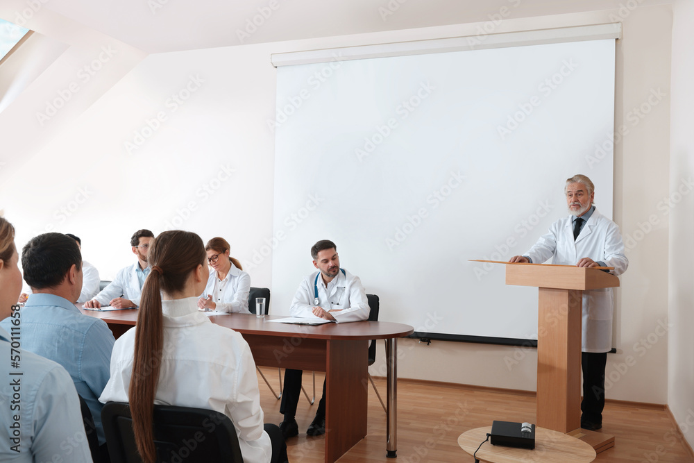 Senior doctor giving lecture in conference room with projection screen Senior doctor giving lecture in conference room with projection screen