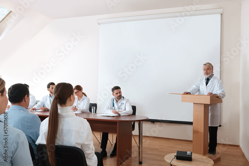 Senior doctor giving lecture in conference room with projection screen