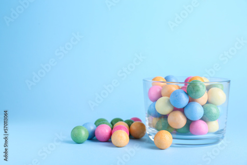 Bowl with bright gumballs on light blue background. Space for text
