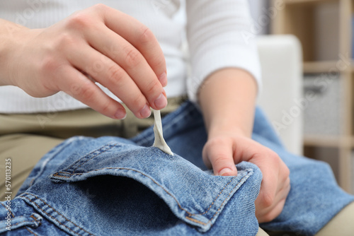 Woman removing chewing gum from jeans indoors, closeup