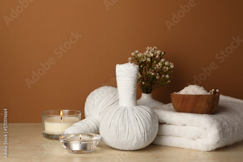Composition with different spa products  candles and flowers on beige table against brown background. Space for text