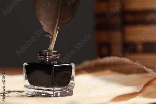 Inkwell with feather and vintage parchments on table, closeup. Space for text