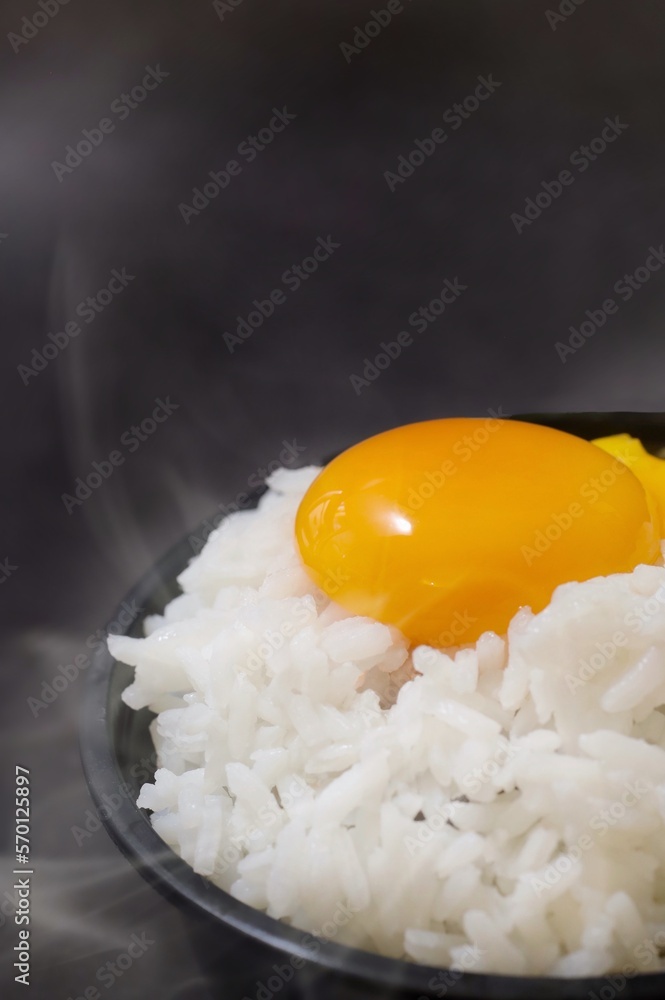 Raw egg on steaming jasmine rice over dark background with smoke in the air , copy space. Raw egg on steaming jasmine rice over dark background with smoke in the air , copy space.