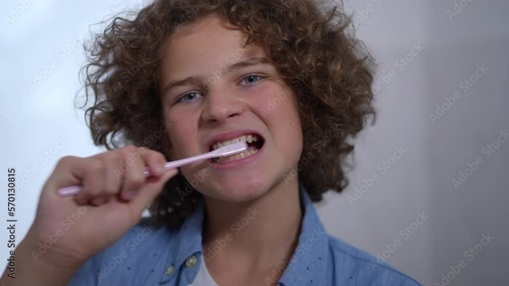 Headshot front view of cute boy brushing teeth and looking at camera with toothy smile. Close-up portrait of charming Caucasian schoolboy posing in bathroom at home in the morning. Daily routine Headshot front view of cute boy brushing teeth and looking at camera with toothy smile. Close-up portrait of charming Caucasian schoolboy posing in bathroom at home in the morning. Daily routine