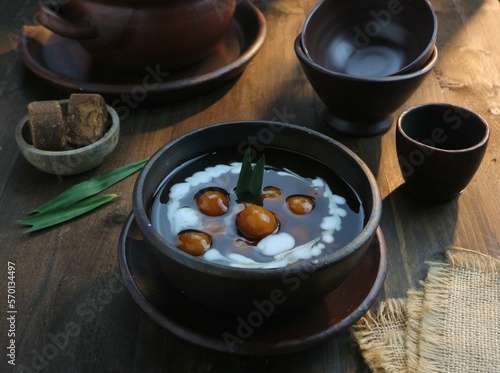 serving a bowl of starch balls with brown sugar sauce and coconut milk on a wooden table