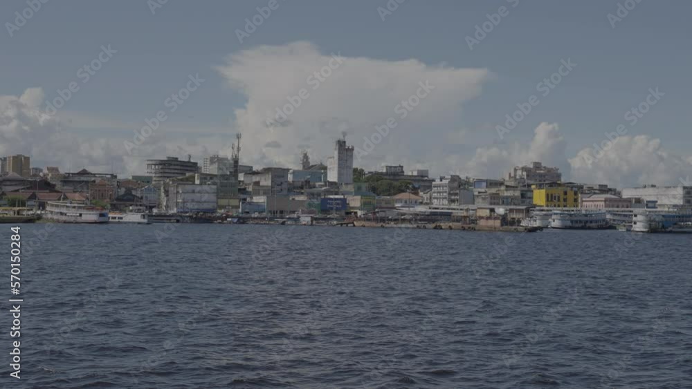 Point Of View Slow Motion Panning Shot Of Residential City Against Cloudy Sky Seen From Wavy Sea On Sunny Day - Manaus, Brazil Point Of View Slow Motion Panning Shot Of Residential City Against Cloudy Sky Seen From Wavy Sea On Sunny Day - Manaus, Brazil